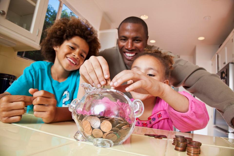 An adult saves coins in a piggy bank with two children.