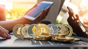 Hot cryptocurrencies to buy: Various cryptocurrency coins are on a computer in front of someone holding a phone.  cryptos for huge profits.  cryptocurrencies to buy