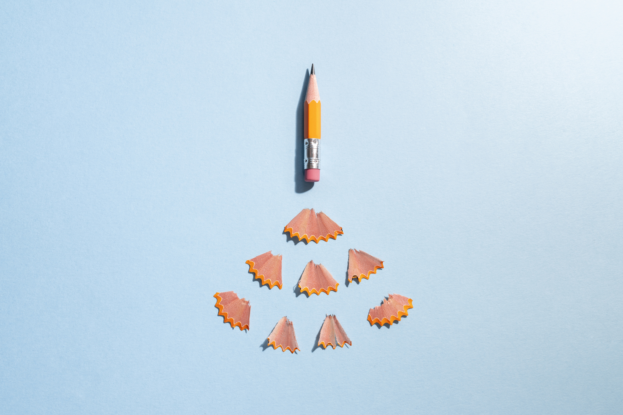 Worn orange pencil on a blue colored background with shavings arranged as if it's a rocket taking off