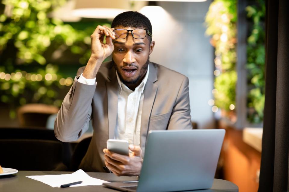 Investor taking off his glasses while looking at his phone in surprise